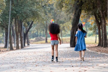 Two multicultural school girls, African-American and Asian kids, walking together hand-in-hand in the park, The moment captures their strong friendship spent weekend free time in natural outdoor
