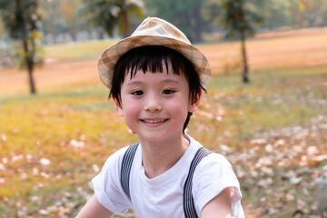 Young Asian boy riding a blue bicycle along a tree-lined park path. He wears a white outfit and hat, pedaling energetically as sunlight summer freedom, fun, and outdoor activities children lifestyle