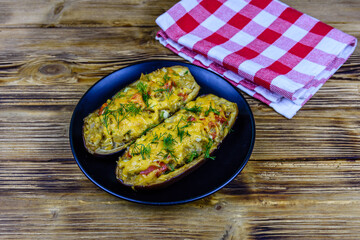 Plate with baked stuffed eggplants on a wooden table