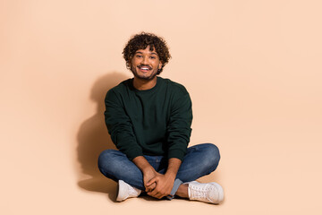 Full size photo of nice young man sit floor wear sweater isolated on beige color background