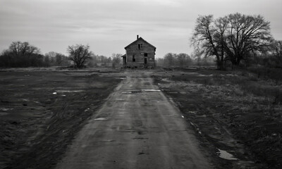 A long, winding dirt road leads to a small house in the middle of a field