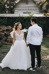 Naklejka premium Stylish groom and beautiful young smiling bride curly blonde in white lace long dress hugging outdoors in village. Wedding photography, portrait.