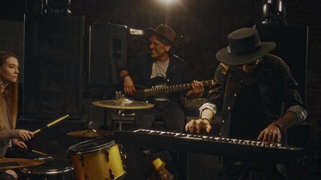 Medium shot of diverse music band mates enjoying jam session while playing percussion,guitar and synthesizer at live performance or concert