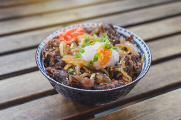 Gyudon Japanese Beef Bowl with Onsen Egg in ceramic bowl on a slatted table in a cafe restaurant.