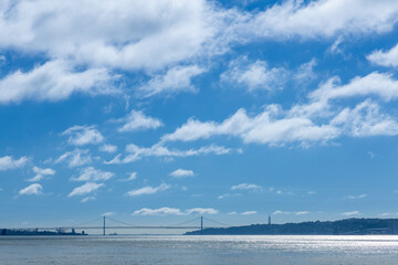 Silhouette view of 25 de Abril Bridge famous tourist landmark of Lisbon connecting Lisboa and Almada over Tagus river. Huge blue sky with clouds.