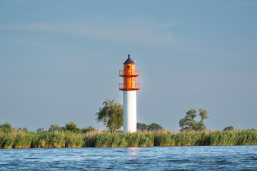 Lighthouse, navigation signs in green reeds under blue sky. Photo from Szczecin Lagoon in Poland.