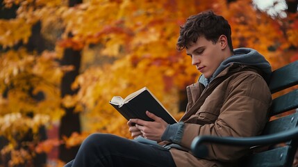A young man sitting alone on a bench, reading a book, with a backdrop of vibrant autumn foliage.