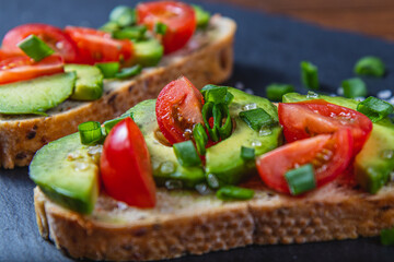 Avocado toast topped with tomato and green onion on a slice of carrot bread
