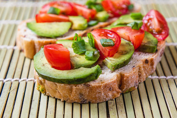 Avocado toast topped with tomato and green onion on a slice of carrot bread