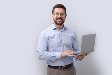 Portrait of smiling businessman with laptop on grey background