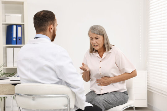 Doctor consulting senior patient with stomach pain in clinic, back view