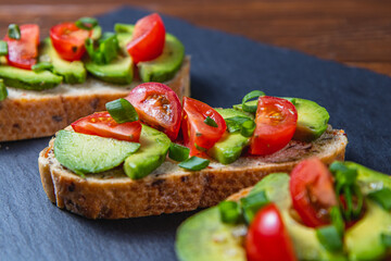 Avocado toast topped with tomato and green onion on a slice of carrot bread