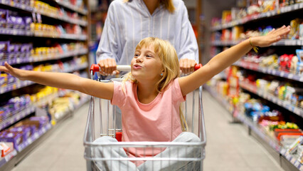 Little girl having fun riding in a shopping cart while shopping groceries at the supermarket with her mother © PeopleVideos