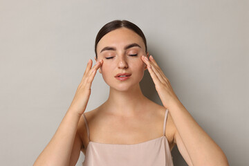 Face massage. Beautiful young woman with healthy skin on grey background