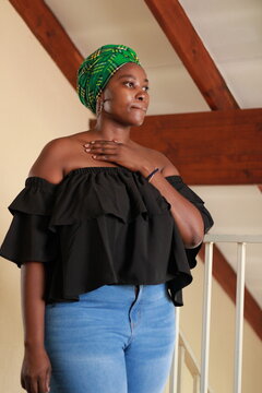 African woman wearing a green doek head wrap with blue denim jeans and black top