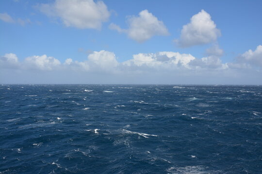 A dynamic view of the ocean with strong waves and choppy waters under a partly cloudy blue sky, showing the intensity of open sea conditions.