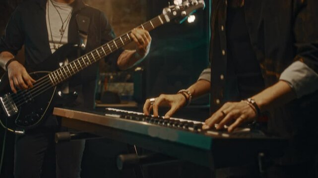Medium tilt of two smiling Caucasian male musicians in casual outfit playing electric guitar and synthesizer in studio, enjoying vibe of live performance