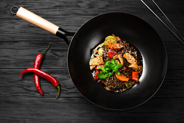 A black wok with a stir fry of vegetables and meat