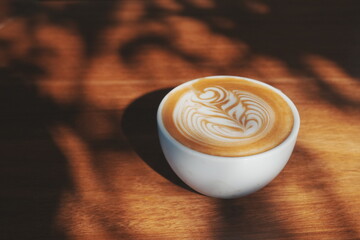 Coffee latte with milk foam made into a flower pattern placed on a wooden table with coffee beans as a decoration. A refreshing morning drink.