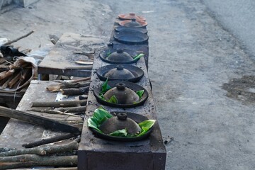 A traditional Indonesian serabi-making process, showing hands pouring batter onto a clay pan over a wood-fired stove. The smoky atmosphere and authentic tools emphasize the local street food culture.