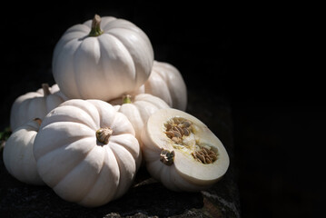 Close-up of white pumpkins standing on a historic stone wall against a dark background. A pumpkin is cut open