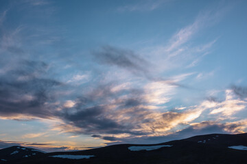 Magnificent sunset cloudy glowing sky of gold colors. Mountain silhouette with snow under dawn skies of sunrise vivid orange tones. Beautiful contrast texture of golden clouds in colorful luminous sky