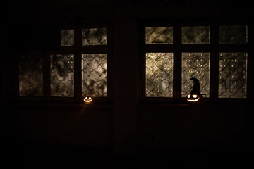 Scary Halloween pumpkin in the mystical house window at night or halloween pumpkin in night on room with blue window. Symbol of halloween in window. Selective focus