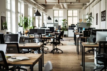 A bright, spacious office filled with modern desks, high-backed chairs, and computers, bathed in natural light from large windows.