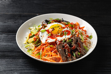 Traditional Korean dish Bibimbap with rice, vegetables beef and egg in a white plate