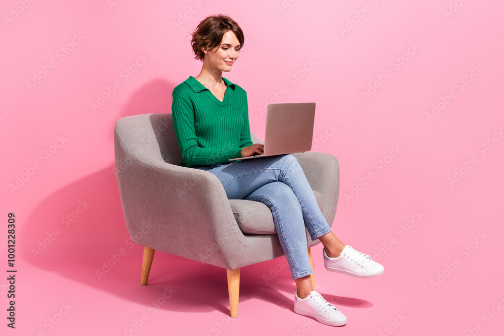 Poster full body shot of young programming woman freelancer sitting in cafeteria armchair using computer is