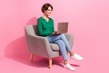 Full body shot of young programming woman freelancer sitting in cafeteria armchair using computer...
