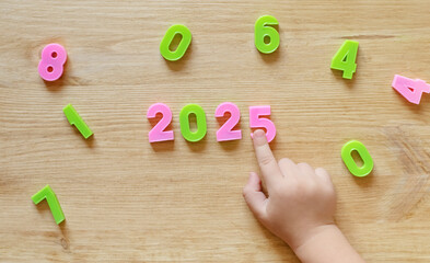 a child lays out the year 2025 in numbers on a wooden board. children's hands close up