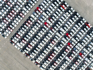 Aerial view of new cars stock at factory parking lot. Above view cars parked in a row. Automotive industry. Logistics business. Import or export new cars at warehouse. Big parking lot at port terminal