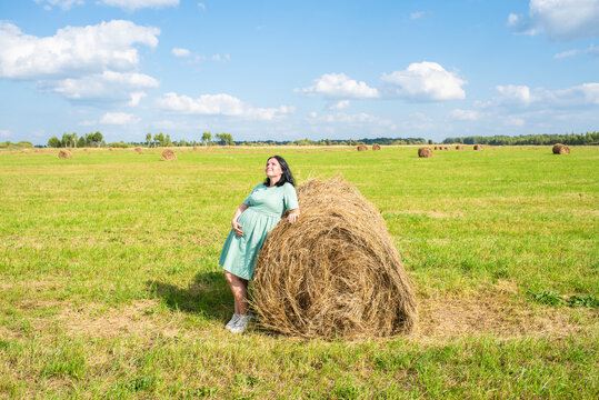 41 year old pregnant woman in the field in front of haystacks, hay rolls. Pregnancy after 40, traveling during pregnancy, summer in the countryside.