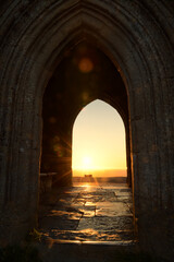 Sunrise framed through a stone archway of a historic Glastonbury Tor tower © PetrDolejsek