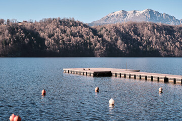 Molo sul lago di Levico con le montagne sullo sfondo e cielo azzurro.