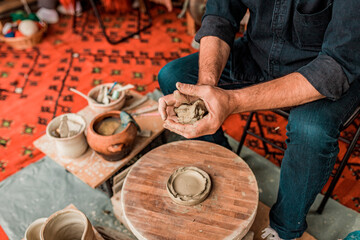 A close-up of hands shaping clay on a pottery wheel, with clay pots visible in the background.