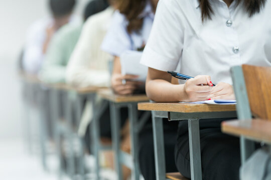 Students Taking Exam in Classroom Setting. Students in uniforms are seated in a classroom, writing answers during an exam, highlighting focus and academic testing.