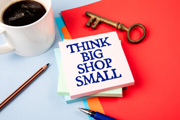 Think Big Shop Small. Notepad with text, coffee mug and golden key on office table
