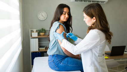 Medical professional wearing gloves administers a vaccine to a young woman in a doctor's office