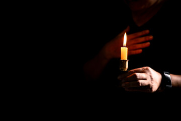In the dark, hand clasped in prayer, illuminated by the soft candlelight, as black flames of candle fire flickered gently. candle, pray, hand, prayer, black, fire, flames, candlelight, light, dark.