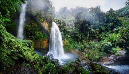 Fototapeta premium A powerful waterfall cascading down a rocky cliff, surrounded by lush tropical foliage. Mist rises from the water, creating a sense of freshness and movement in the dense jungle.