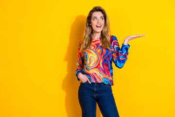 Photo of young shocked funky woman wearing colorful pullover and hold arm looking great deal isolated on yellow color background