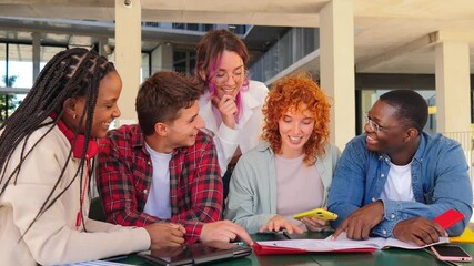 Diverse group of college teenage students studying together, looking at notes and using a cellphone while collaborating at university campus library in a cheerful, casual setting. Five people teamwork - Powered by Adobe