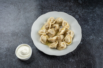 A plate of dumplings sits on a table next to a small bowl of sour cream