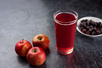 A glass of red liquid is poured into a glass next to a bowl of blueberries