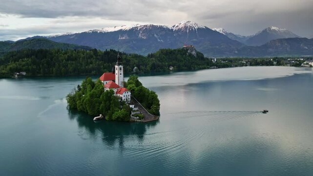 Aerial view of Bled lake and boat with the Pilgrimage Church of the Assumption of Maria on a small island after sunset, Slovenia, 4k