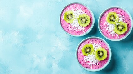 Three vibrant bowls of pink smoothie topped with kiwi slices and shredded coconut, set against a pale blue background.