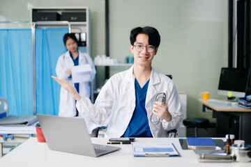 Obraz premium Confident young male doctor in white medical uniform sit at desk working on computer