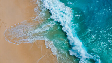 A stunning aerial shot capturing waves crashing onto a golden sandy beach, showcasing the contrast between the vibrant turquoise water and the soft shoreline.